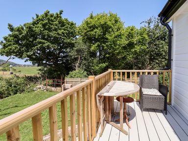 An outdoor balcony with a wooden railing a folding table and a wicker chair with a cushion at Melbecks in Abergele