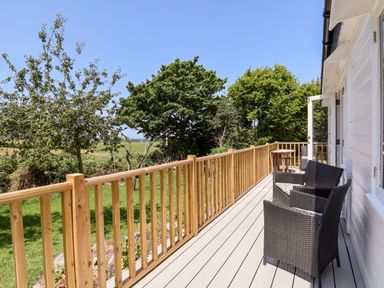 A wooden balcony with black wicker chairs and a small table overlooking trees and grass at Melbecks in Abergele