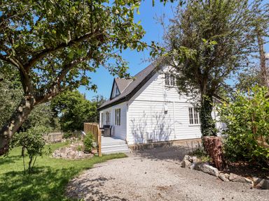 A white house with a sloped roof and a porch surrounded by trees and a gravel driveway at Melbecks in Abergele