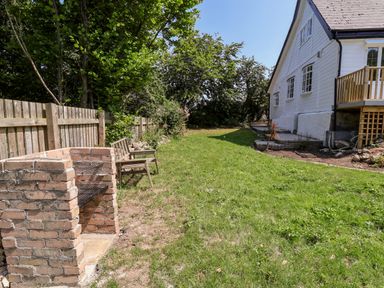 A backyard with a brick barbecue and wooden bench next to a wooden fence and a white house at Melbecks Abergele