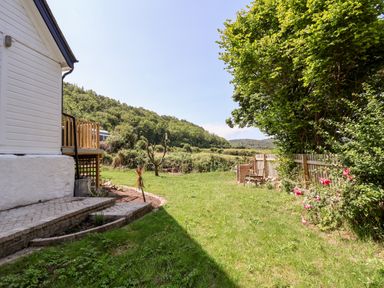 A grassy backyard with a wooden fence flowers a patio area and a tree at Melbecks in Abergele