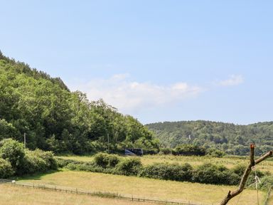 A rural landscape with green fields trees hills a road and a fenced area at Melbecks in Abergele