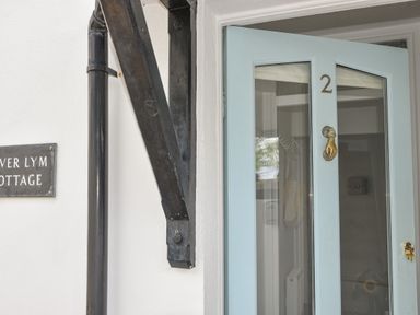 A light blue door with glass panels and a brass door knocker beside a white wall with a black rainwater pipe at River Lym Cottage Lyme Regis