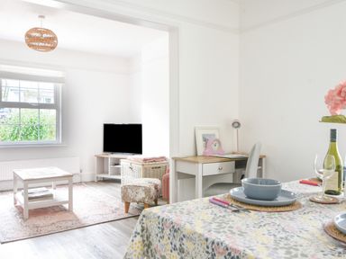 A dining table with plates and wine next to a desk and a living room with a coffee table and TV at River Lym Cottage in Lyme Regis
