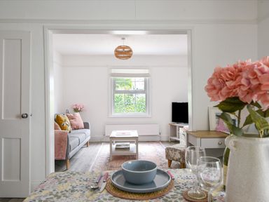 A living room with a gray sofa and pink cushions next to a window and a coffee table at River Lym Cottage Lyme Regis