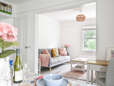 A living room with a gray sofa pink cushions and a coffee table next to a dining table with blue bowls and a wine bottle at River Lym Cottage Lyme Regis