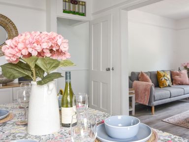 A dining table with pink flowers and wine bottle next to a living room with a gray sofa at River Lym Cottage Lyme Regis