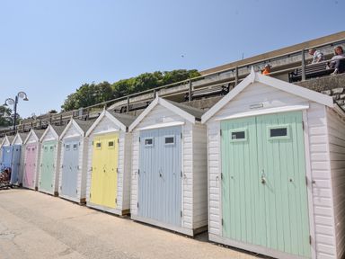 A row of small beach huts with pastel colored doors on a paved area at River Lym Cottage in Lyme Regis