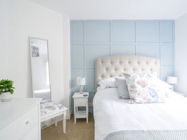 A bedroom with a bed with patterned pillows and a blue paneled wall at River Lym Cottage in Lyme Regis