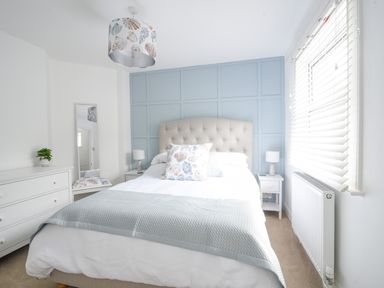 A bedroom with a bed bedside tables a chest of drawers a mirror and a window with blinds at River Lym Cottage in Lyme Regis