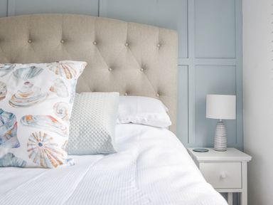 A bed with patterned and textured pillows and a bedside table with a lamp at River Lym Cottage Lyme Regis