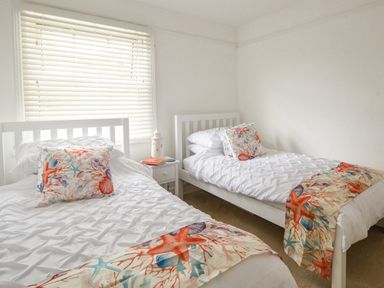 A bedroom with two single beds with white bedding and colorful sea-themed pillows and throws at River Lym Cottage in Lyme Regis