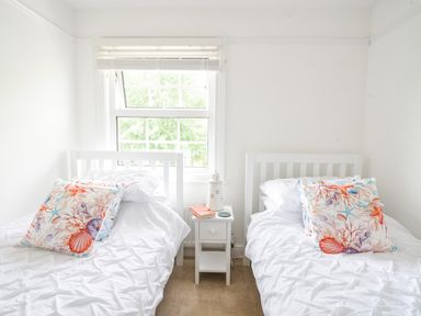 A bedroom with two single beds white bedding and colorful pillows and a small white nightstand with a lamp and books at River Lym Cottage Lyme Regis