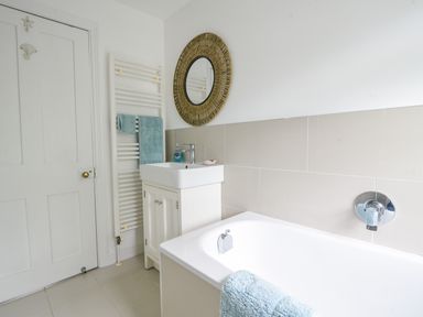 A bathroom with a white bathtub and sink with a round mirror above at River Lym Cottage in Lyme Regis