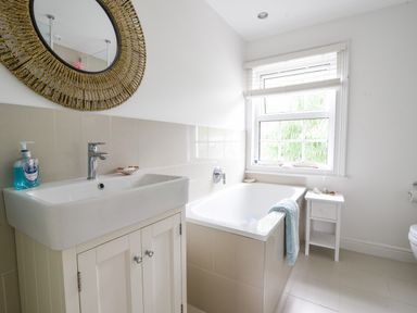 A bathroom with a sink a bathtub a small white side table and a window at River Lym Cottage in Lyme Regis