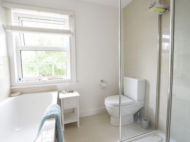 A bathroom with a bathtub a window a small table a toilet and a shower at River Lym Cottage Lyme Regis