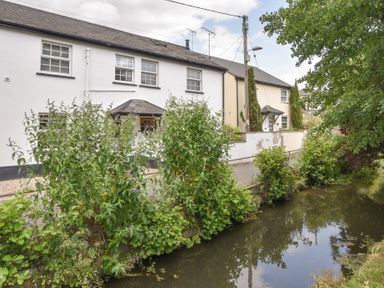 A river flowing beside a row of houses with bushes and trees at River Lym Cottage Lyme Regis