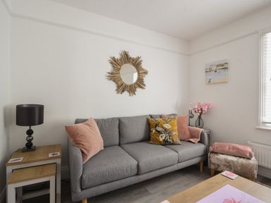 A living room with a gray sofa pillows a side table lamp and wall mirror at River Lym Cottage in Lyme Regis
