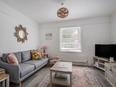 A living room with a gray sofa a coffee table a television and a window at River Lym Cottage in Lyme Regis