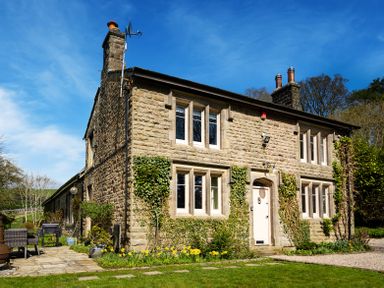 A stone house with multiple windows ivy growing on the walls a white door and a garden with flowers at The Lodge in Hartlington near Grassington