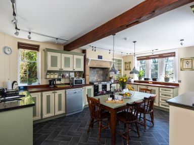 A kitchen with a wooden dining table and chairs a stove and cabinets with windows showing outside at The Lodge in Hartlington near Grassington