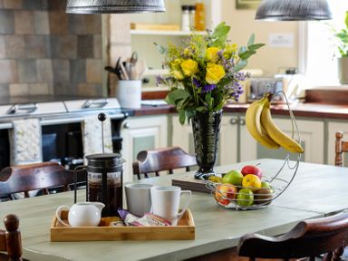A kitchen table with a coffee press two mugs a vase of flowers and a fruit basket at The Lodge Hartlington near Grassington