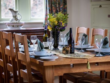 A wooden dining table with chairs set with wine glasses plates and napkins and a flower vase at The Lodge in Hartlington near Grassington