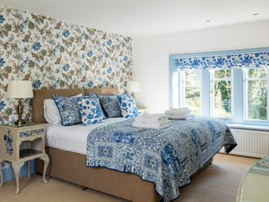 A bedroom with a large bed and bedside tables with lamps and a window with blue floral curtains at The Lodge in Hartlington near Grassington