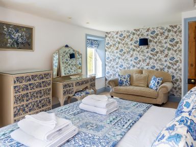 A bedroom with a bed with folded towels a floral dresser and vanity and a beige sofa with cushions at The Lodge in Hartlington near Grassington