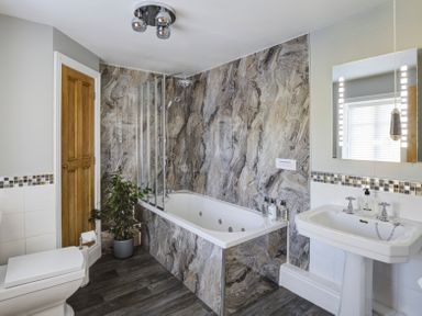 A bathroom with a bathtub a shower a sink a toilet a plant and a mirror at The Lodge Hartlington near Grassington
