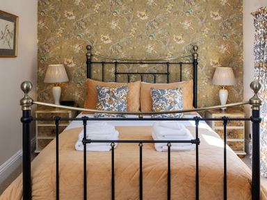 A bedroom with a metal bed frame brown bedding patterned pillows nighttime lamps and floral wallpaper at The Lodge in Hartlington near Grassington