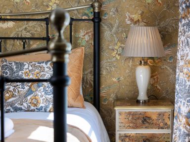 A bedroom corner with a metal bed frame, patterned pillows, a bedside table with drawers, and a lamp at The Lodge in Hartlington near Grassington