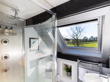 A bathroom with a glass shower enclosure a window overlooking trees and grass and a sink with a towel rack at The Lodge in Hartlington near Grassington
