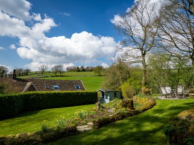 A garden with a lawn chairs and table near trees and a shed at The Lodge in Hartlington near Grassington