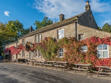 Stone building with climbing plants and outdoor wooden picnic tables at The Lodge in Hartlington near Grassington