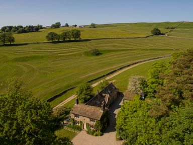 A countryside house with trees and green fields surrounding it at The Lodge in Hartlington near Grassington