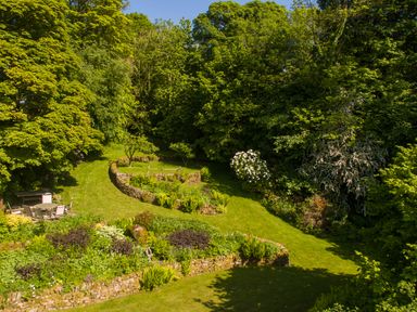 A garden with stone walls trees and outdoor seating at The Lodge in Hartlington near Grassington