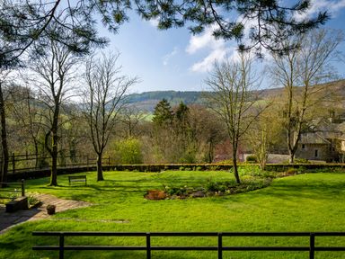 A garden with grass trees a bench and distant hills at Kail House in Grassington