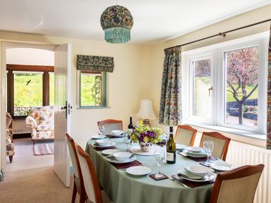 A dining room with a table set for six and floral decorations at Kail House in Grassington