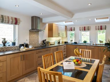 A kitchen with wooden cabinets a dining table with fruit and a note and windows with striped blinds at Kail House in Grassington