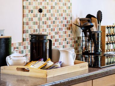 A kitchen countertop with a wooden tray holding a French press coffee maker sugar bowl packets mugs and a milk jug at Kail House in Grassington