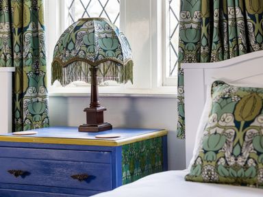 A bedside table with a decorative lamp next to a bed with patterned cushions and matching curtains at Kail House in Grassington