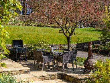 An outdoor patio with a dining table and chairs chimney and barbecue on a stone patio at Kail House in Grassington