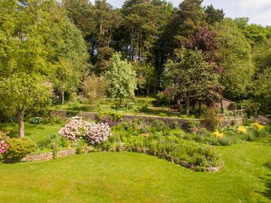 A garden with grass lawn flower beds trees and a stone wall at Kail House in Grassington