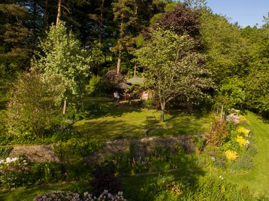 A garden with a stone wall flowers various trees and a bench at Kail House in Grassington