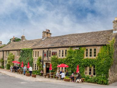 An outdoor seating area with people sitting under red umbrellas outside a stone building with ivy on the walls at Kail House in Grassington