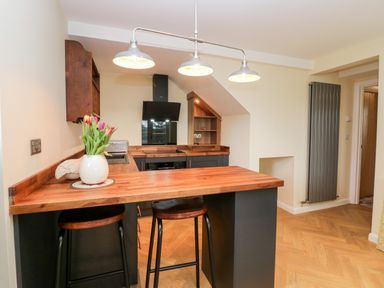 A kitchen with wooden countertops bar stools and flowers on a table at How Hill Farm Cottage in Greystoke