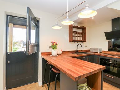 A kitchen with wooden countertops bar stools and a half open black door at How Hill Farm Cottage in Greystoke