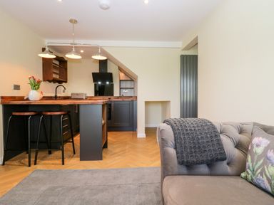 A kitchen with black cabinets and wooden countertops next to a gray sofa with a knitted throw at How Hill Farm Cottage in Greystoke