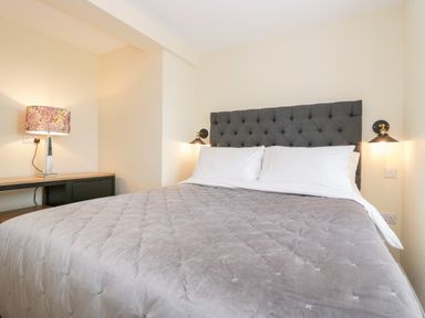 A bedroom with a bed with a grey headboard and bedspread and a lamp on a wooden table at How Hill Farm Cottage in Greystoke